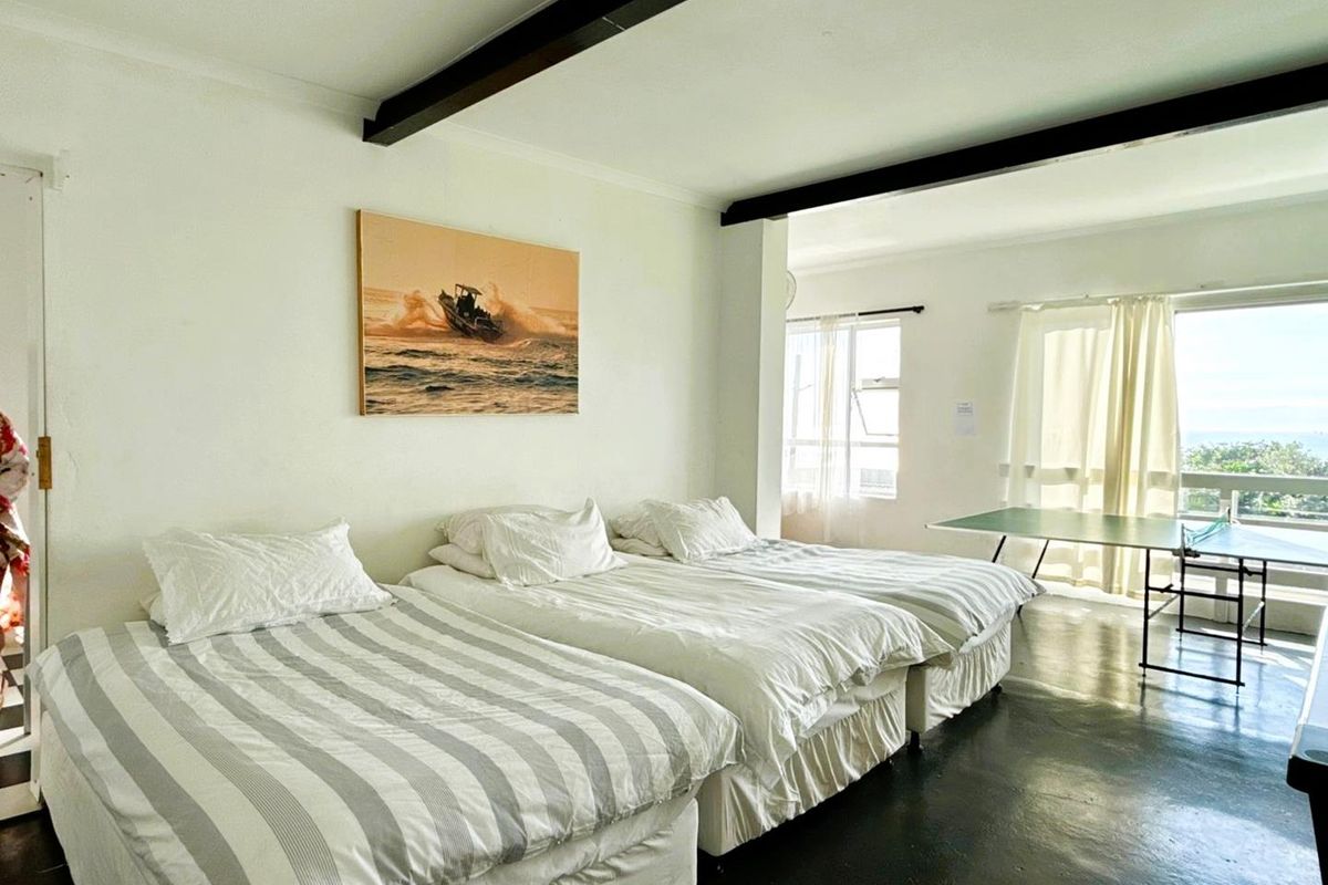 Spacious bedroom featuring exposed ceiling beams, polished concrete flooring, and large windows providing natural light and access to an outdoor area.