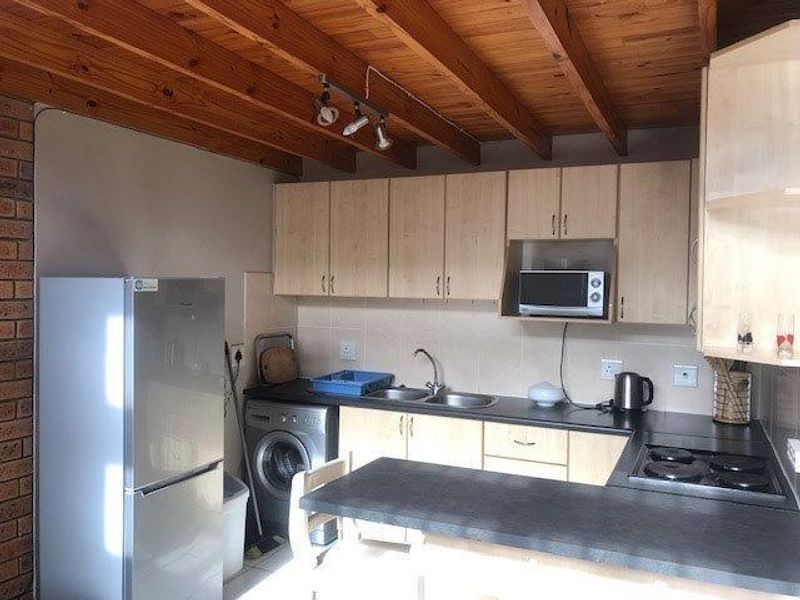 Functional kitchen featuring light wood cabinetry, exposed timber ceiling beams, dark countertops, built-in microwave, and an electric hob with a tiled backsplash.