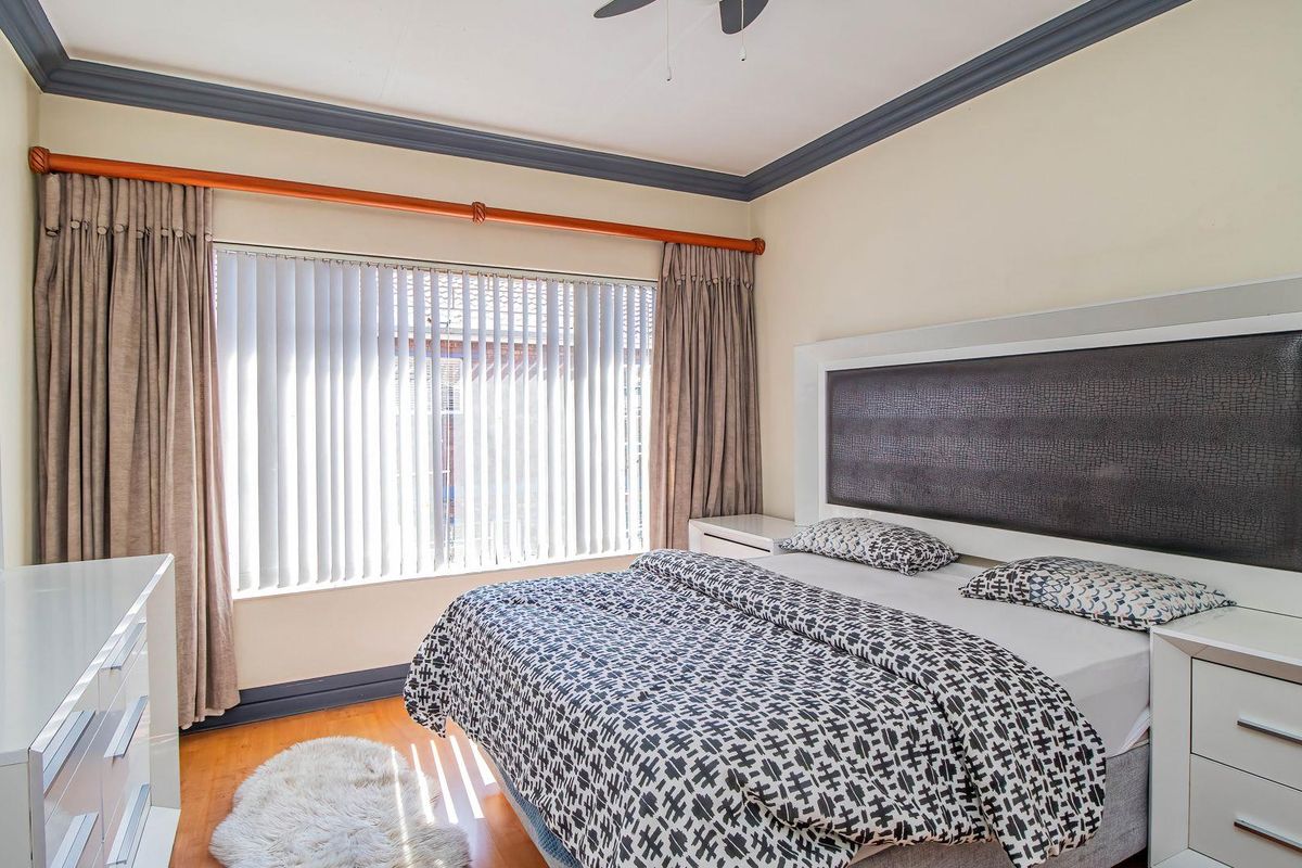 A well-lit bedroom featuring laminate flooring, crown molding, and a ceiling fan, offering a comfortable and functional living space.