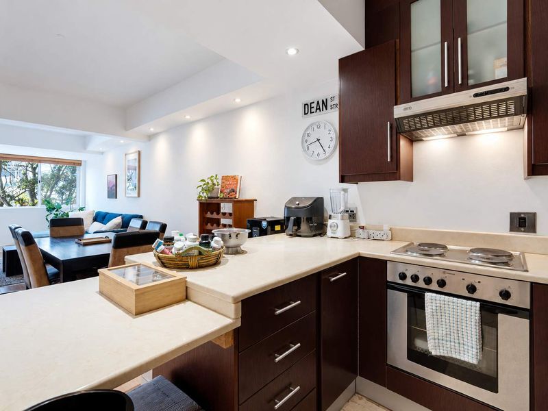Open-plan kitchen and living area featuring dark wood cabinetry, integrated appliances, stone countertops, and recessed lighting, creating a functional and cohesive living space.