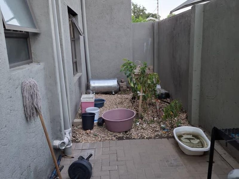 A rear exterior courtyard area featuring paved flooring, boundary walls, and an external geyser installation.