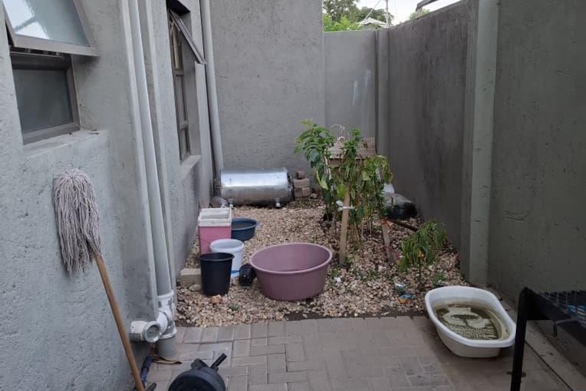 A rear exterior courtyard area featuring paved flooring, boundary walls, and an external geyser installation.