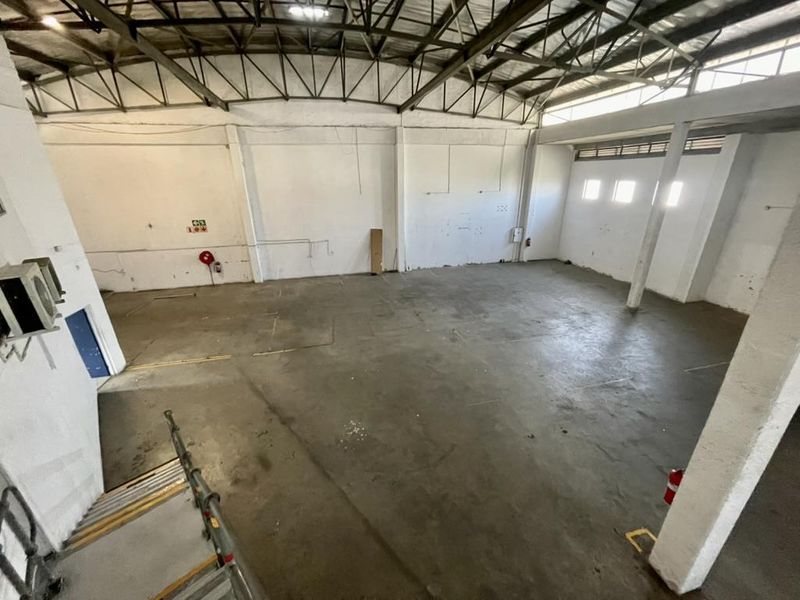 Spacious industrial warehouse unit featuring high ceilings with exposed steel trusses, concrete flooring, and functional fire safety equipment.