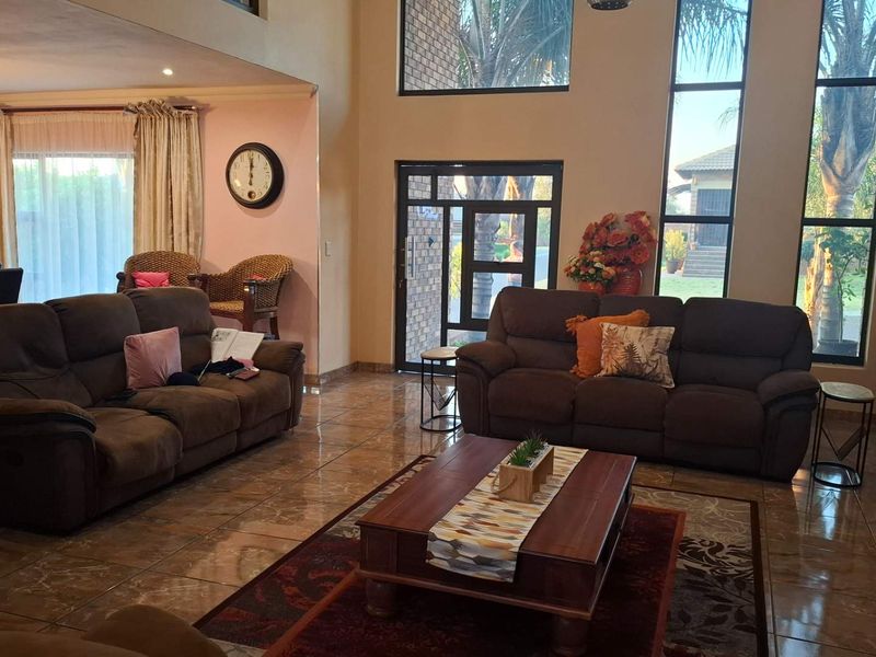 Spacious living room featuring double volume windows, tiled flooring, and recessed lighting, creating an open and airy atmosphere with natural light.