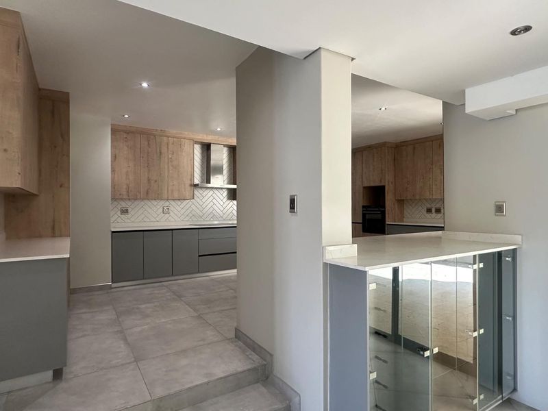 Modern kitchen featuring two-tone cabinetry, stone countertops, herringbone backsplash, built-in oven, and extractor fan, finished with large format floor tiles.