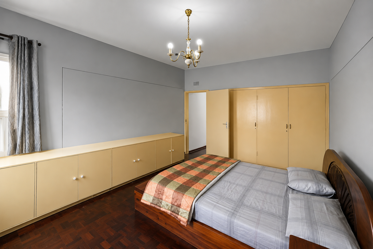 Spacious bedroom featuring built-in storage cabinetry, parquet flooring, and a classic chandelier, offering a functional layout with neutral wall tones.