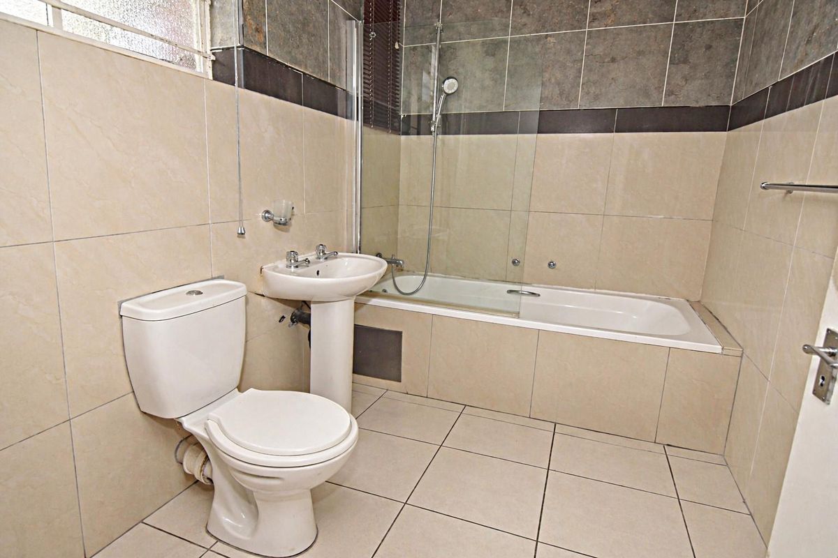 A functional bathroom featuring a pedestal basin, a toilet, and a bathtub with a glass shower screen and tiled wall finishes.