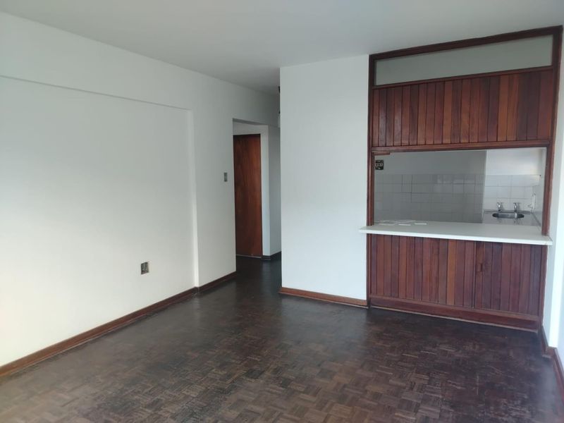 Open plan living area featuring dark parquet flooring and a timber-paneled kitchen pass-through with a service counter.
