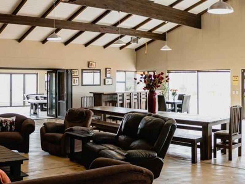 Spacious open-plan living area featuring exposed timber ceiling beams, tiled flooring, and a seamless flow to the outdoor patio through large sliding doors.
