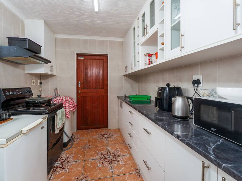 A functional kitchen featuring white cabinetry, dark laminate countertops, tiled backsplash, and tiled flooring, providing a practical workspace with direct exterior access.