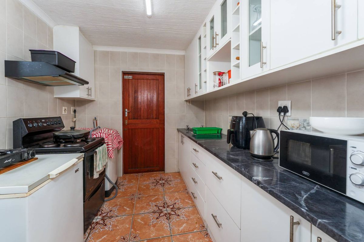 A functional kitchen featuring white cabinetry, dark laminate countertops, tiled backsplash, and tiled flooring, providing a practical workspace with direct exterior access.