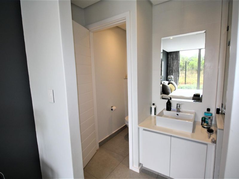 Modern bathroom featuring a sleek vanity with a vessel sink, wall-mounted mirror, and a separate enclosed toilet area with neutral floor tiling.