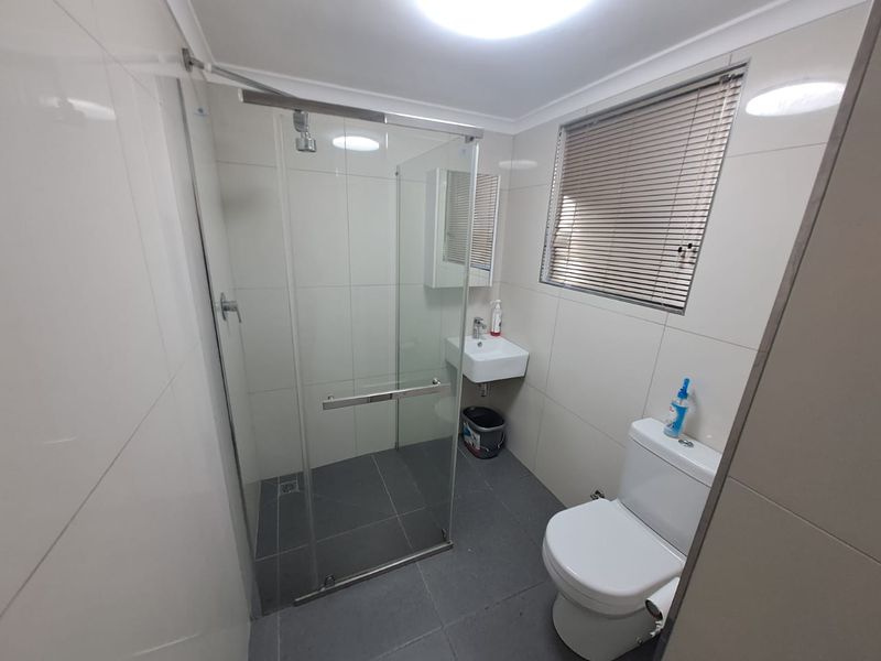A clean, modern bathroom featuring a glass-enclosed shower, wall-mounted basin, toilet, and neutral tiled finishes throughout.