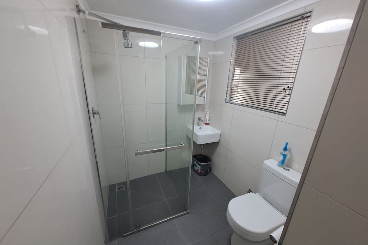A clean, modern bathroom featuring a glass-enclosed shower, wall-mounted basin, toilet, and neutral tiled finishes throughout.