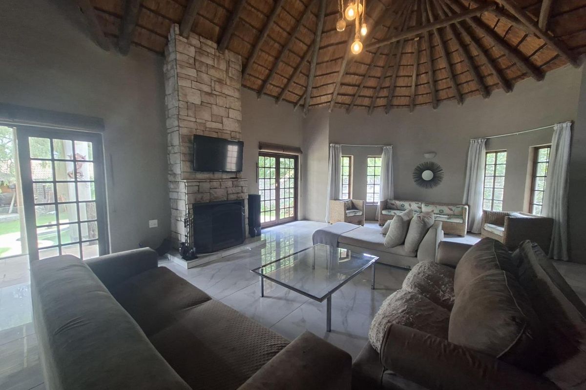 Spacious living room featuring a high thatched ceiling, stone-clad fireplace, and large glass doors leading to the garden.