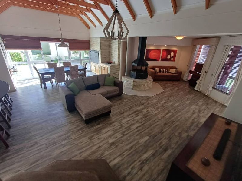 Spacious open-plan living and dining area featuring high vaulted timber-beamed ceilings, a central freestanding fireplace, and large windows providing ample natural light.
