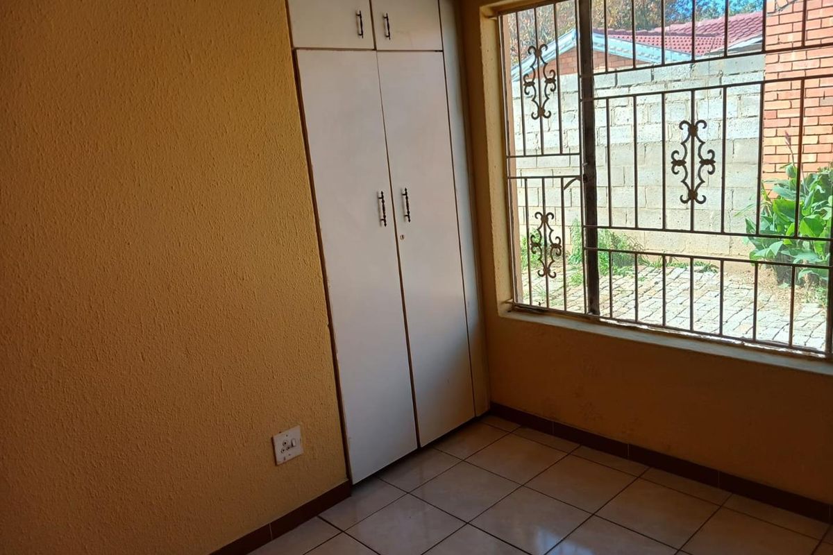 An empty bedroom featuring built-in cupboards, tiled flooring, and security bars on the window, providing a functional space ready for personalization.