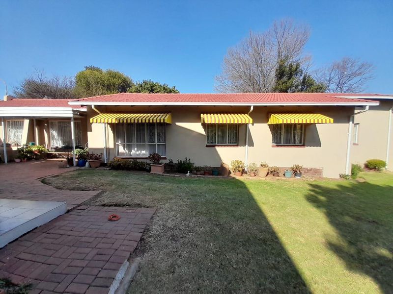 Rear view of the house featuring a tiled roof, brick paved patio area, and yellow striped window awnings overlooking a lawn.