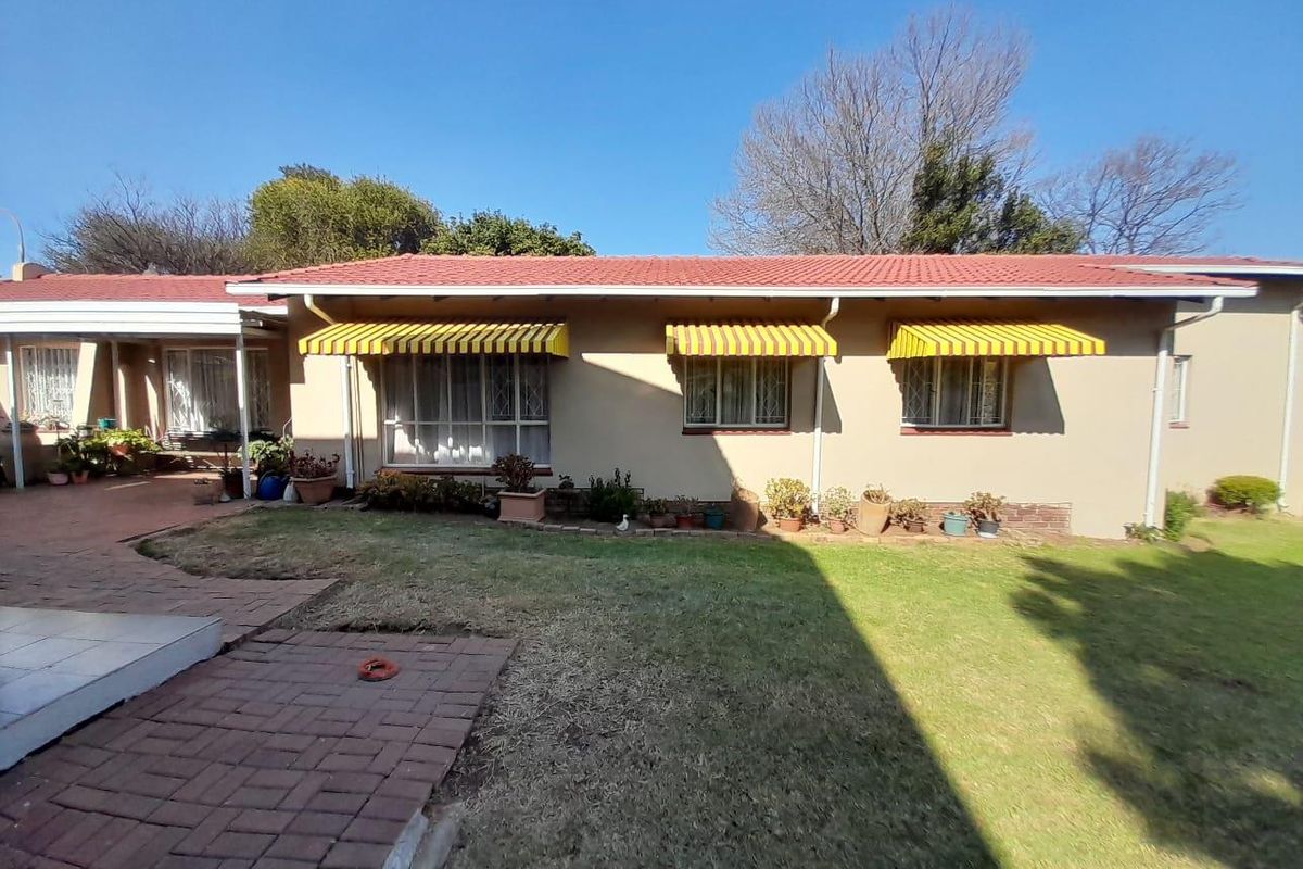 Rear view of the house featuring a tiled roof, brick paved patio area, and yellow striped window awnings overlooking a lawn.
