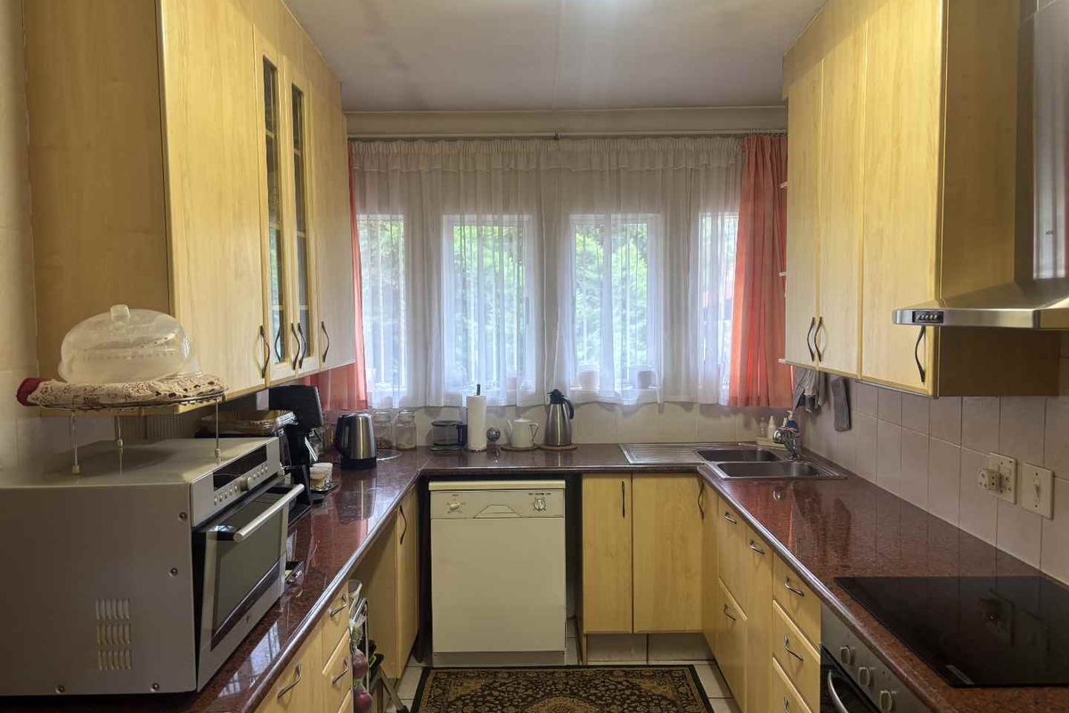 A functional galley-style kitchen featuring laminate cabinetry, granite-look countertops, a built-in oven, and a stainless steel extractor fan.