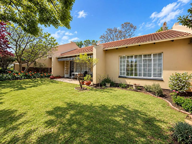 A well-maintained rear exterior view featuring a paved patio, retractable awning, and a lush, landscaped garden with established trees.