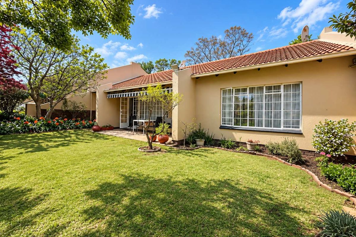 A well-maintained rear exterior view featuring a paved patio, retractable awning, and a lush, landscaped garden with established trees.