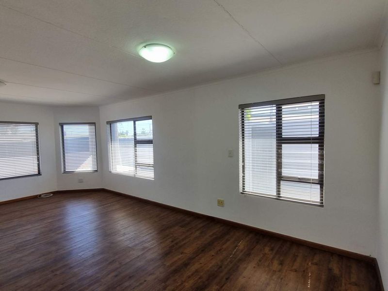 A bright and spacious living area featuring modern laminate flooring, large windows with fitted blinds, and neutral wall finishes.