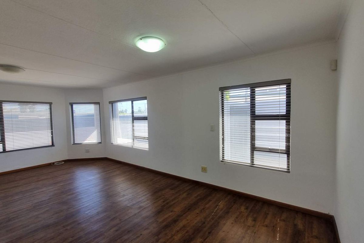 A bright and spacious living area featuring modern laminate flooring, large windows with fitted blinds, and neutral wall finishes.