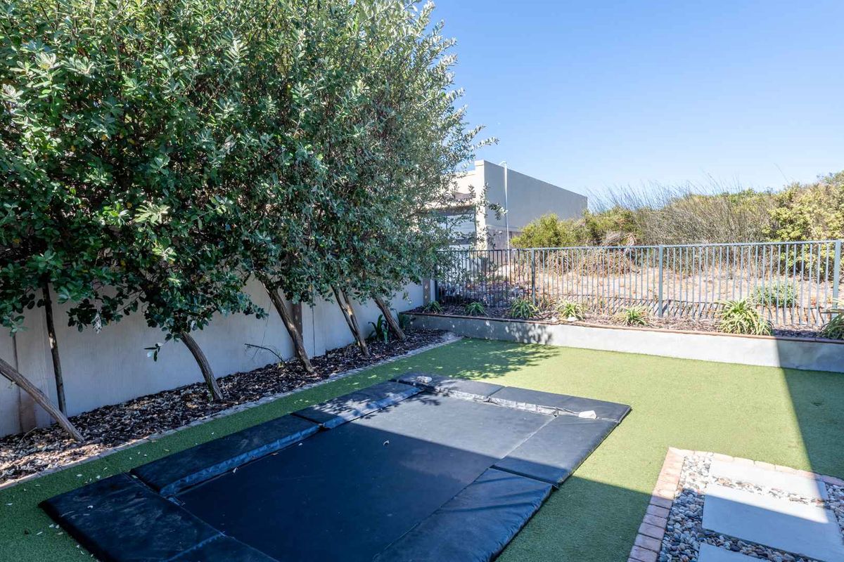 A private rear garden area featuring artificial turf, a sunken trampoline, perimeter walling, and metal fencing.