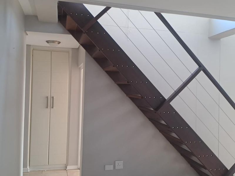 A bright hallway featuring a modern open-tread staircase with metal railings and a built-in storage cupboard with neutral tiled flooring.