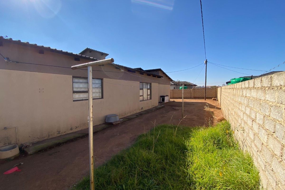 Rear exterior view of the property featuring a concrete block boundary wall, metal washing line, and a basic garden area with exposed soil.