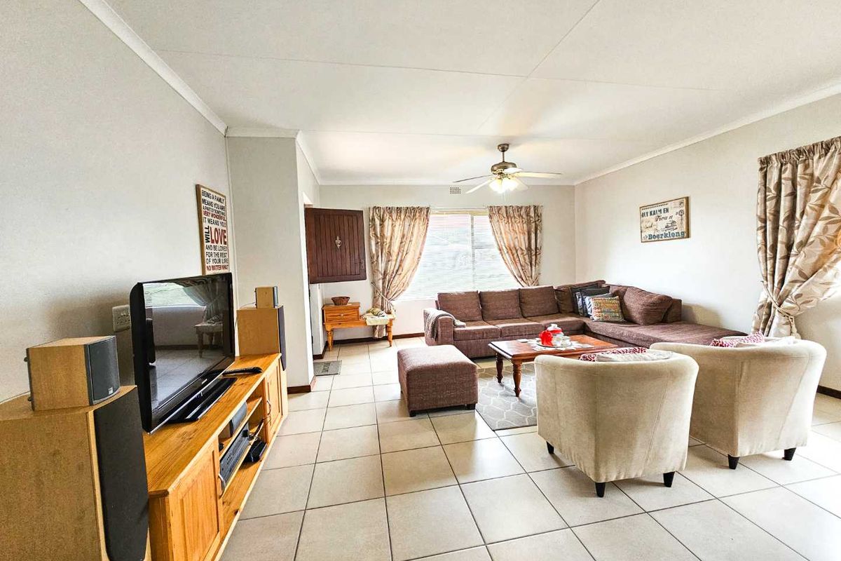 Spacious living room featuring neutral ceramic floor tiles, a ceiling fan, and large windows allowing for natural light.