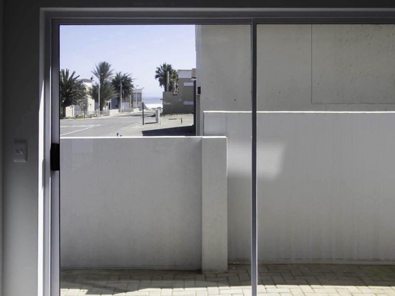 A view from inside looking out through a sliding glass door onto a paved patio area with a masonry wall and street view beyond.