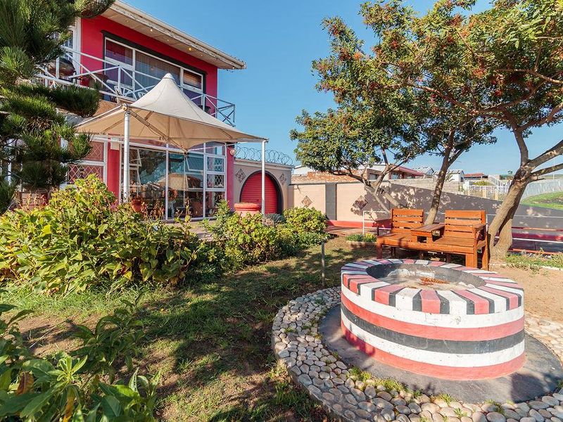 Rear garden area featuring a paved patio, built-in fire pit, and a tensioned shade sail structure adjacent to the main house.
