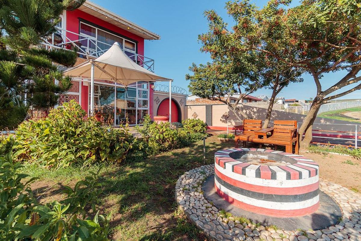 Rear garden area featuring a paved patio, built-in fire pit, and a tensioned shade sail structure adjacent to the main house.