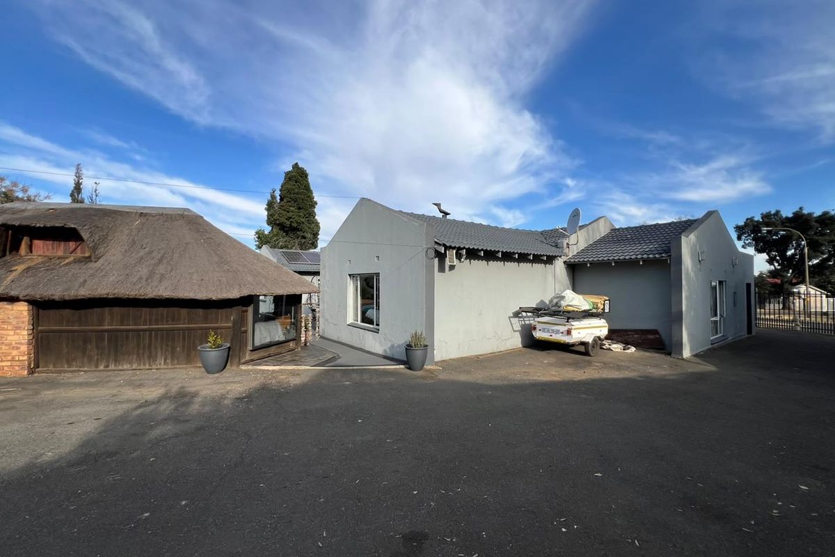 Rear view of the property featuring a combination of tiled and thatched roof structures with an expansive asphalt driveway area.