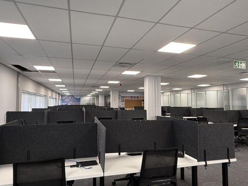 Open-plan office space featuring a suspended ceiling with recessed LED lighting, glass partitioning, and carpeted flooring.