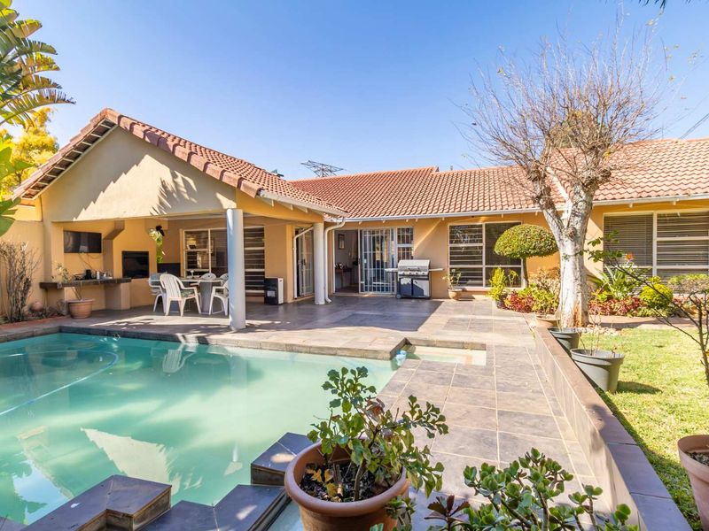 A well-maintained outdoor entertainment area featuring a swimming pool, spacious tiled patio, and a built-in braai, perfect for relaxed outdoor living.
