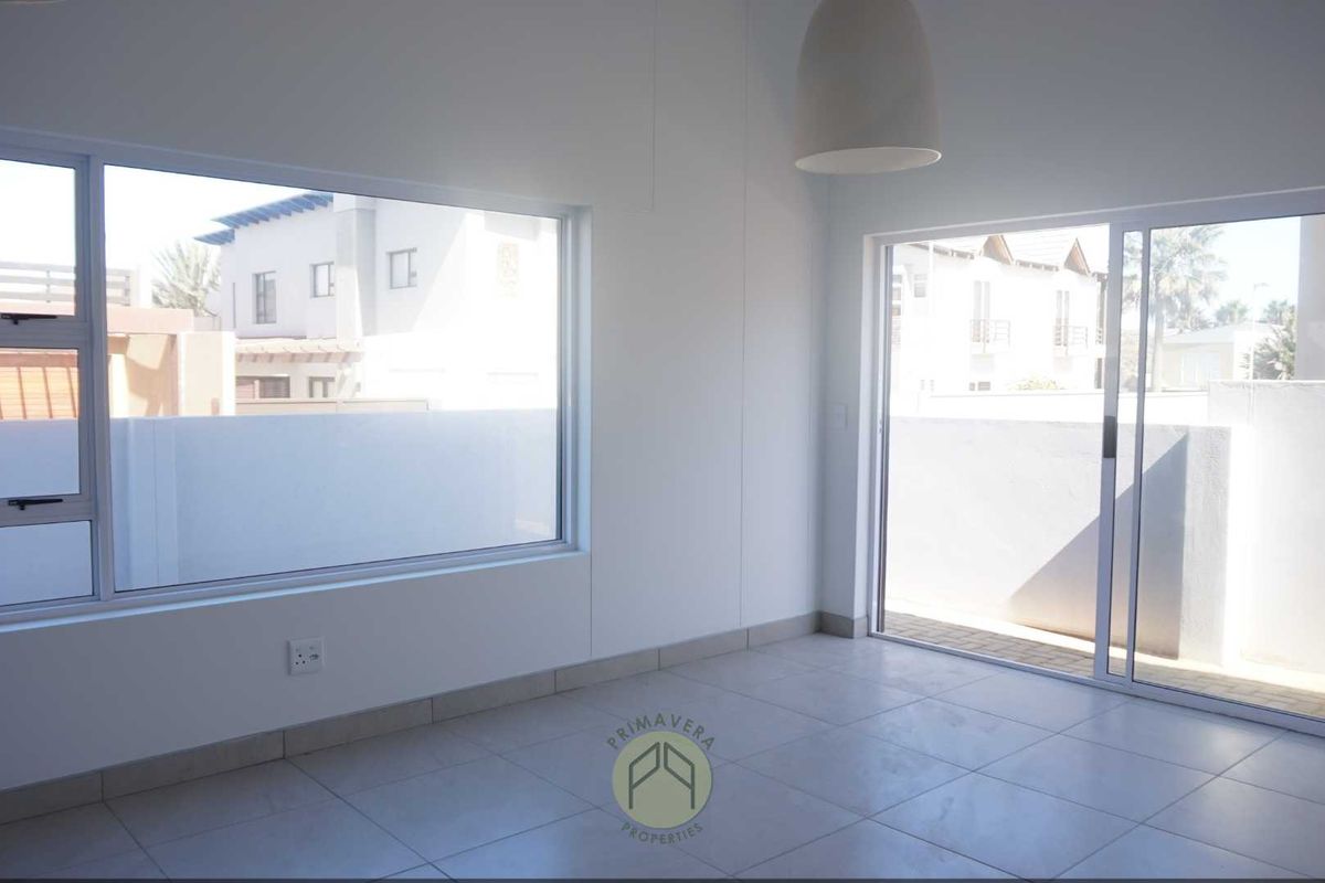 A bright, empty living area featuring large windows, a sliding glass door leading to the exterior, and neutral tiled flooring.