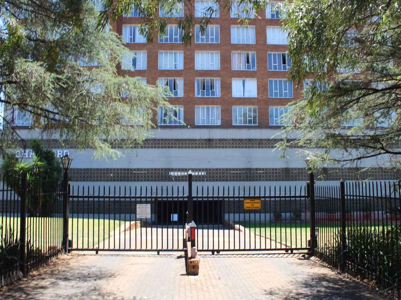 Front view of a multi-story brick apartment building featuring secure gated access and perimeter fencing.