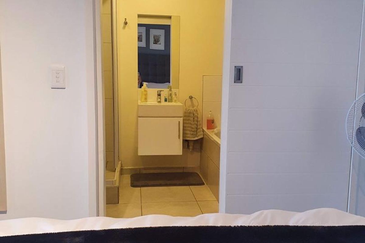 An en-suite bathroom featuring a sliding door, vanity cabinet, shower enclosure, and built-in bathtub, accessible directly from the bedroom.