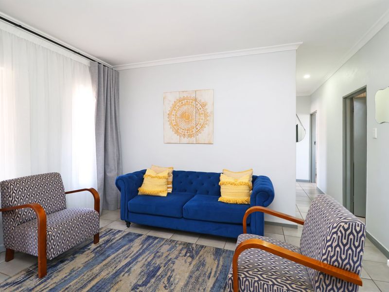 A bright and well-maintained living room featuring neutral tiled flooring, coved ceilings, and large windows with curtain tracks.