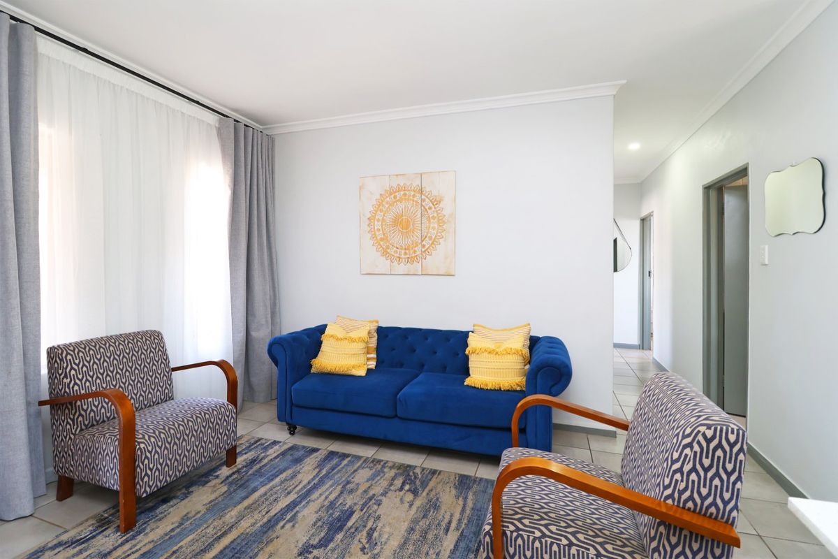 A bright and well-maintained living room featuring neutral tiled flooring, coved ceilings, and large windows with curtain tracks.