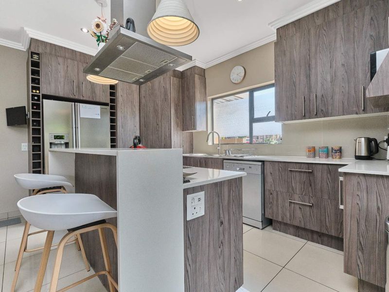 Modern kitchen featuring wood-grain cabinetry, stone countertops, a central island with breakfast bar, and integrated extractor fan.
