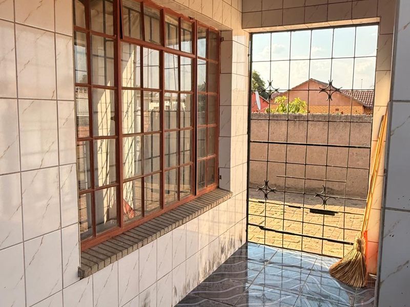 A covered patio area featuring tiled walls and flooring, with an exposed ceiling structure requiring finishing and general maintenance to improve the space.