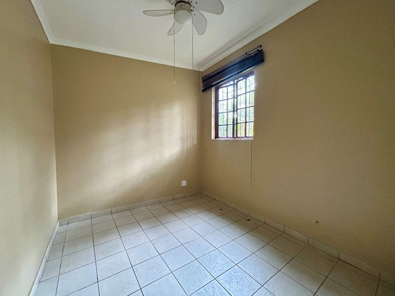An empty bedroom featuring tiled flooring, a ceiling fan, and a window with security bars, offering a blank canvas for personalization.