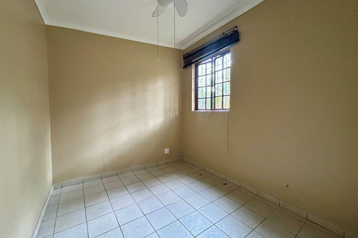 An empty bedroom featuring tiled flooring, a ceiling fan, and a window with security bars, offering a blank canvas for personalization.