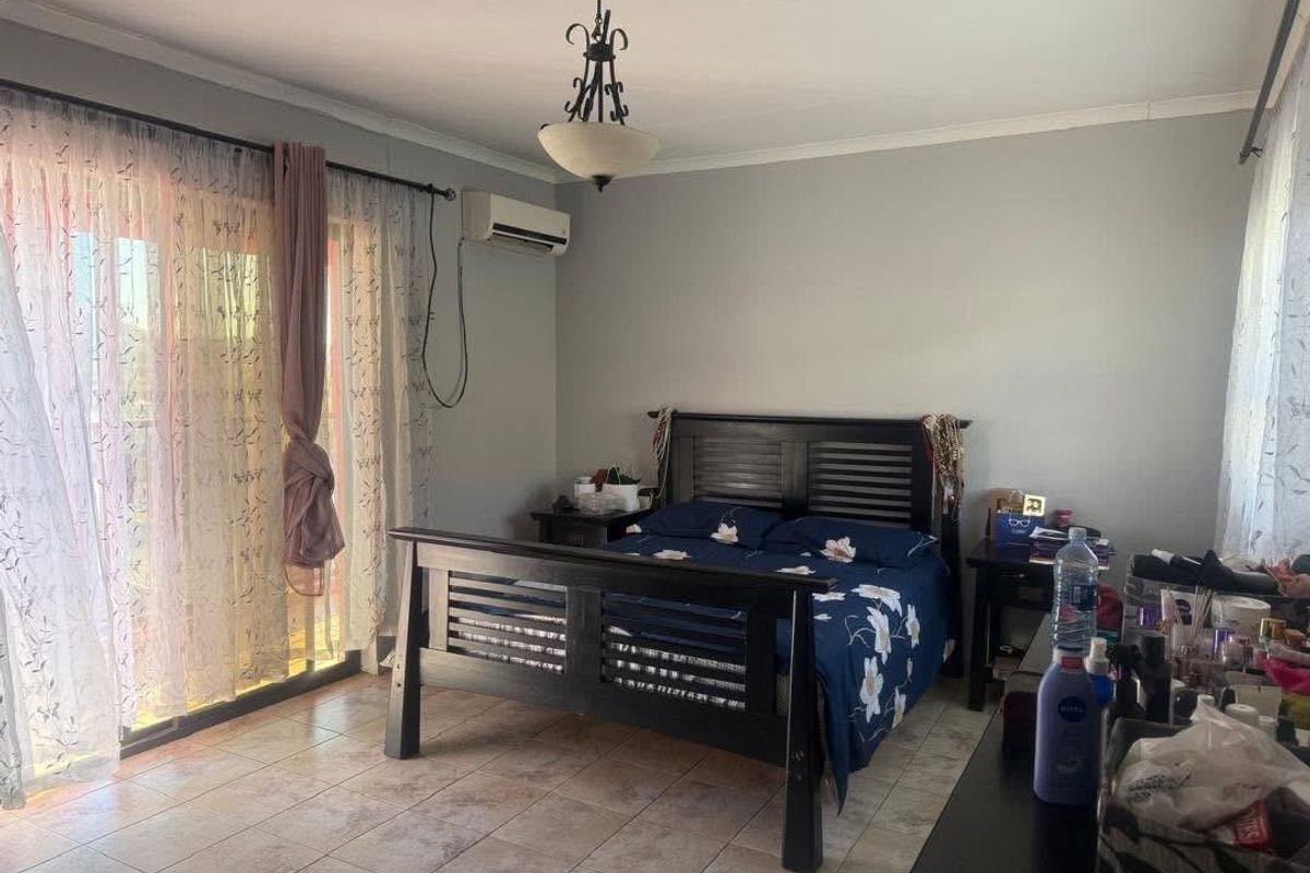 A spacious bedroom featuring tiled flooring, a wall-mounted air conditioning unit, and sliding glass doors providing access to an outdoor area.