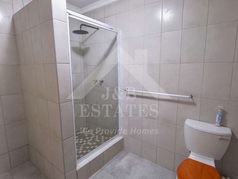 A functional bathroom featuring a tiled shower enclosure with a rain shower head and a standard toilet.
