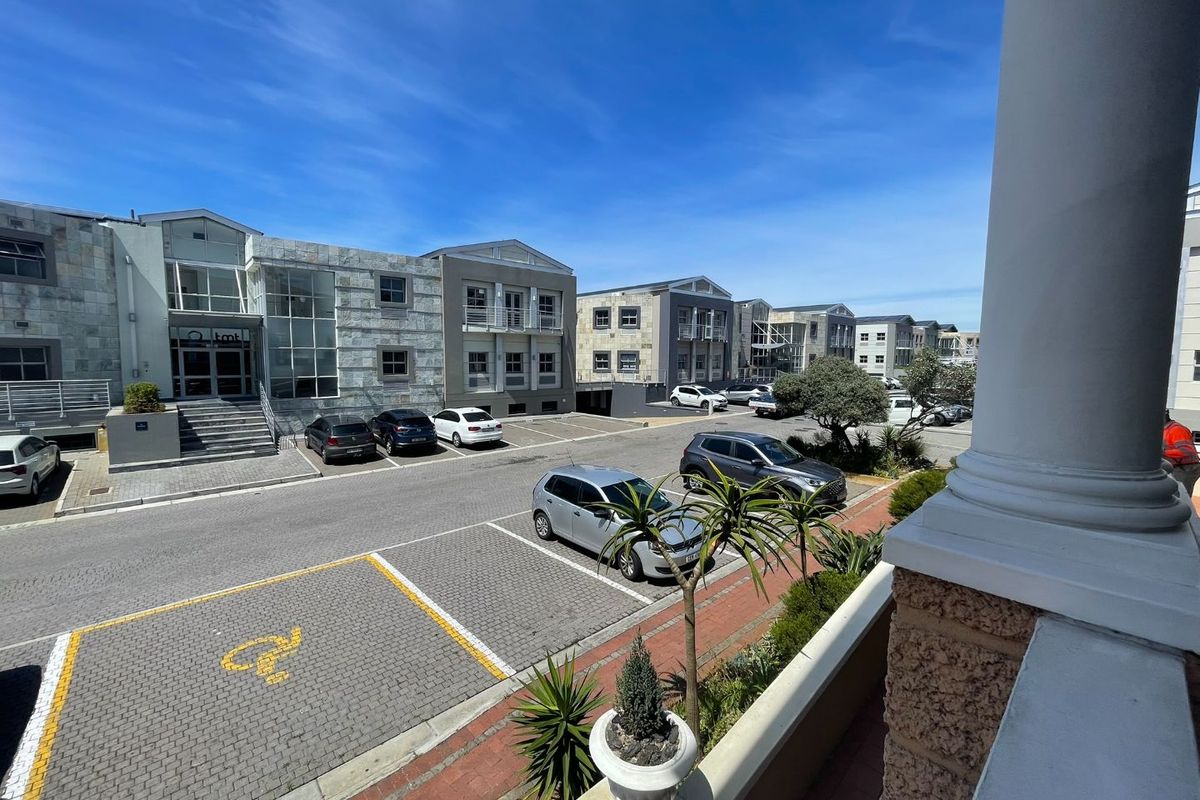 View of the office complex exterior featuring stone-clad buildings, paved parking bays, and a balcony overlooking the grounds.